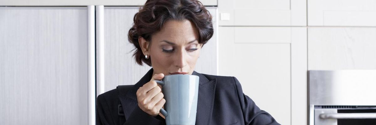 sietésben lévő nő reggel egy bögre kávéval és egy aktatáskával a kezében gyűrű az ujján női szmokingban kisminkelve a konyhában