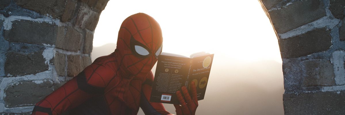 Spider-Man leaning on concrete brick while reading book