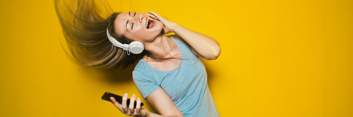 Telefonról fülhallgatóval zenét hallgató fiatal nő sárga háttér előtt